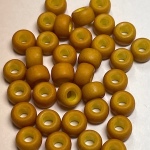 May include: A collection of small, round, wooden beads in a warm, golden-brown hue. Each bead has a central hole and a slightly lighter yellow interior. The beads are scattered across a white surface.