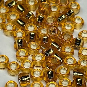 May include: A large quantity of small, round, amber-colored glass beads with gold accents. The beads have a hole in the center for stringing.