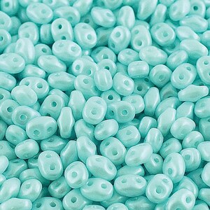 May include: A close-up shot of a pile of light blue, oval-shaped beads. Each bead has two holes for stringing. The beads have a pearlescent finish, giving them a subtle shine. These beads are ideal for jewelry making.
