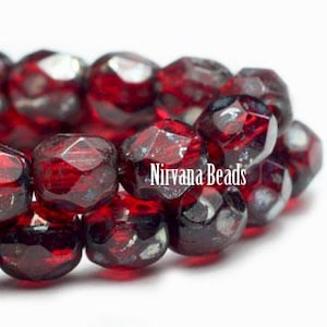 May include: A strand of deep red, faceted glass beads with a translucent finish. The beads are arranged in a cluster, reflecting light off their multiple angled surfaces. The text Nirvana Beads is printed in white across the center of the image.