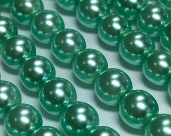 May include: Rows of light green, glossy, round beads. The beads are evenly spaced and reflect light, creating highlights. The beads are likely for jewelry making or crafting.