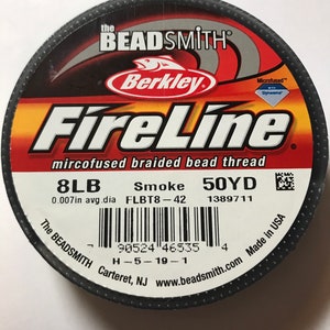 May include: A spool of black FireLine microfused braided bead thread by Berkley Beadsmith. The spool is labeled with the text "8LB", "Smoke", "50YD", "0.007in avg. dia", "FLBT8-42", "1389711", "The Beadsmith", "Carteret, NJ", "www.beadsmith.com", "H-5-19-1", and "Made in USA".