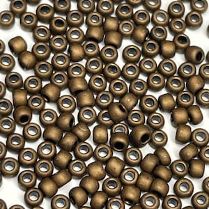 May include: A large quantity of small, round, matte bronze beads. The beads have a hole in the center and are scattered on a white surface.