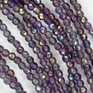 May include: A strand of iridescent purple glass beads with a faceted finish. The beads are small and round, and they have a subtle shimmer.
