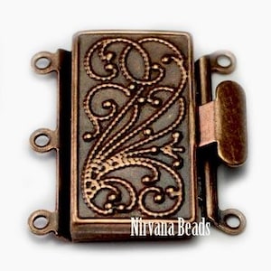 May include: A rectangular copper-toned metal jewelry clasp featuring an intricate raised scrollwork pattern on the front surface. The clasp includes three small circular loops on one side and a single locking mechanism on the other. Text reads Nirvana Beads.