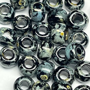 May include: A collection of black and white ceramic beads with a speckled pattern. The beads have a hole in the center for stringing.