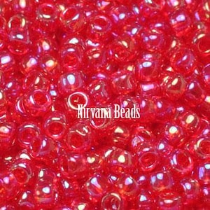 May include: Close-up of a pile of small, round, red beads with a glossy finish. The beads are scattered, filling the frame. The text "Nirvana Beads" is printed in white, slightly curved, across the center of the image.
