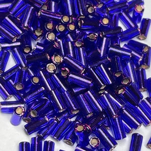May include: A pile of small, iridescent blue glass beads. The beads are cylindrical in shape and have a metallic sheen.