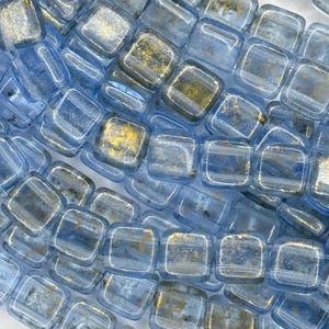 May include: A strand of square glass beads with a light blue color and gold flecks. The beads are translucent and have a slightly iridescent finish.