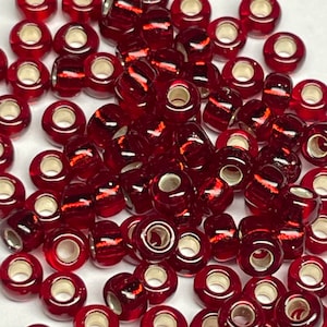 May include: A pile of red glass seed beads with silver-toned metal caps. The beads are round and have a slightly iridescent finish.