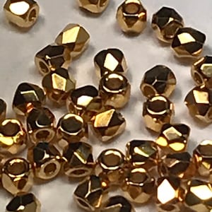 May include: A collection of gold-colored faceted beads. The beads are small and have a shiny finish.