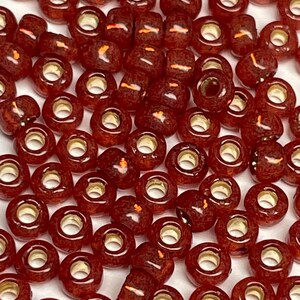 May include: A large pile of small, round, red glass beads with gold accents. The beads have a slightly translucent quality and are perfect for jewelry making or other craft projects.