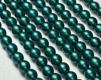 May include: A strand of teal green round beads. The beads are smooth and have a metallic sheen.