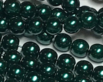 May include: Close-up of several strands of dark green, glossy beads. The beads are round and evenly sized, reflecting light. The image highlights the beads' smooth texture and deep color, suggesting they are for jewelry making or crafting.