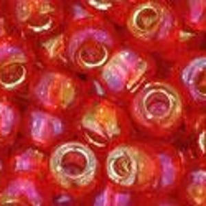May include: Close-up of a collection of small, round, red beads. The beads have a glossy finish with hints of gold and pink. Each bead has a hole running through the center, suggesting they are for stringing or crafting projects.