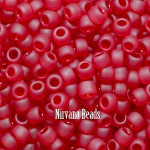 May include: Close-up of a pile of small, opaque, red seed beads. The beads are cylindrical with a hole through the center. The text "Nirvana Beads" is printed in white.