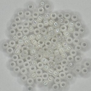 May include: A large quantity of small, white, round seed beads. The beads have a hole in the center and a slightly iridescent finish.