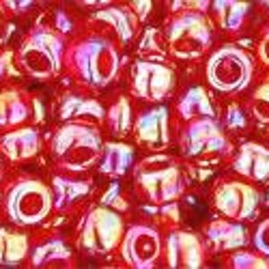 May include: Close-up of a pile of small, round, red beads. The beads have a glossy finish with iridescent highlights of pink and gold. Each bead has a hole running through the center.