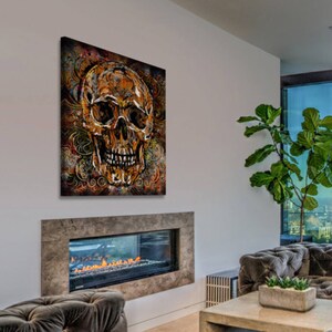 May include: A gold skull with intricate details is painted on a canvas with a dark brown background and swirling patterns. The skull has a dark brown eye socket and a white background.
