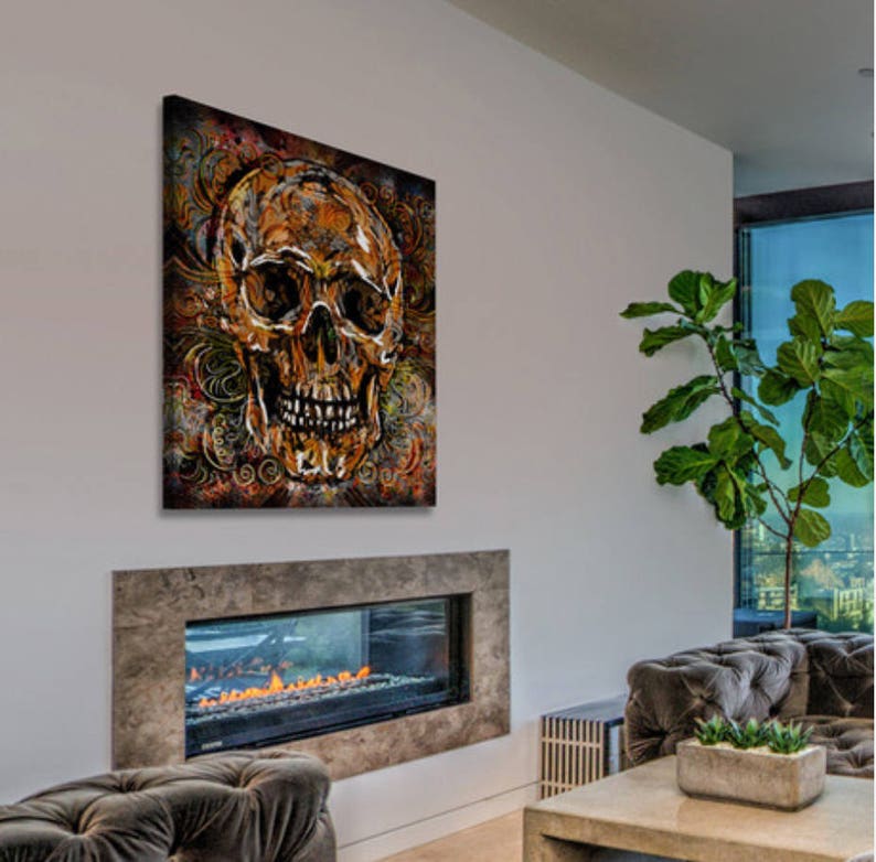 May include: A gold skull with intricate details is painted on a canvas with a dark brown background and swirling patterns. The skull has a dark brown eye socket and a white background.