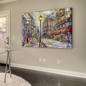 Pode incluir: Uma pintura abstrata colorida que representa uma cena de rua parisiense com um poste de luz no centro. Os edif&iacute;cios s&atilde;o pintados em tons de vermelho, amarelo e azul. A rua &eacute; ladeada por pessoas e lojas.