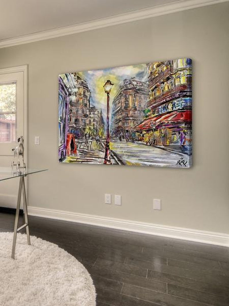 Pode incluir: Uma pintura abstrata colorida que representa uma cena de rua parisiense com um poste de luz no centro. Os edif&iacute;cios s&atilde;o pintados em tons de vermelho, amarelo e azul. A rua &eacute; ladeada por pessoas e lojas.