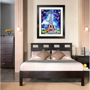 May include: A framed painting of the Eiffel Tower in Paris, France. The painting is done in a colorful abstract style with a blue background and white snowflakes. The painting is hanging on a wall in a bedroom with a dark wood bed frame and white bedding.