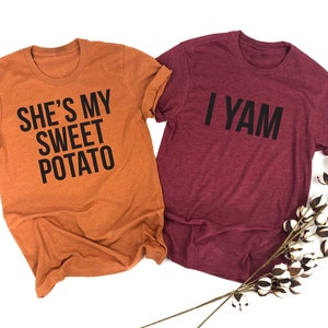 May include: Two t-shirts with a Thanksgiving-themed couple's design. The orange shirt says "She's my sweet potato" and the maroon shirt says "I yam".