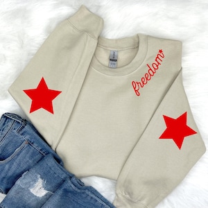 May include: A beige sweatshirt with red star accents on the sleeves and the word "freedom" in red script on the right shoulder.