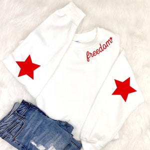 May include: White sweatshirt with red stars on the sleeves and the word "freedom" embroidered on the front.