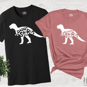 May include: Two t-shirts, one black and one pink, with a white dinosaur graphic and the text "Daddy/Mommy Saurus Rex".