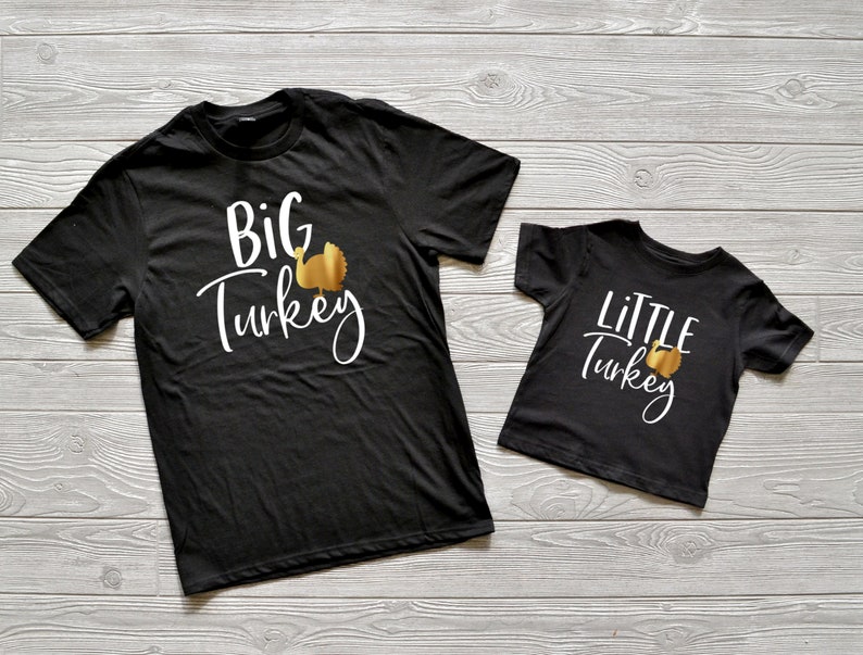 May include: Two black t-shirts with a gold turkey graphic and white text. The larger shirt says "BIG TURKEY" and the smaller shirt says "LITTLE TURKEY".