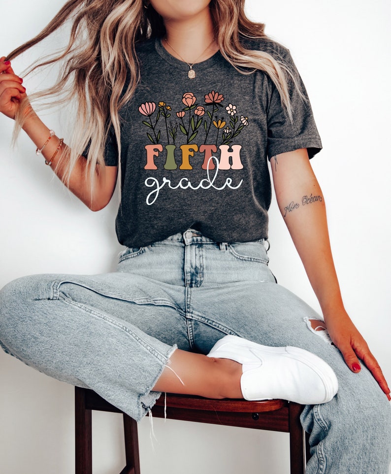 May include: A gray t-shirt with a floral design and the text "FIFTH grade" in colorful letters.