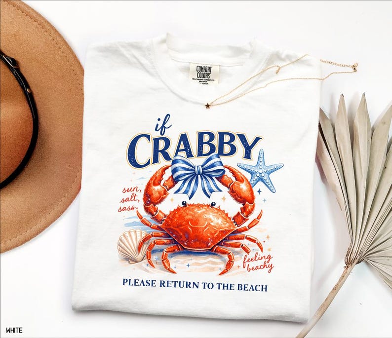 May include: White t-shirt with a crab graphic. The crab is red with a blue bow, and the text reads "if CRABBY" and "PLEASE RETURN TO THE BEACH". A starfish and seashell are also featured in the design. The shirt is a Comfort Colors brand.