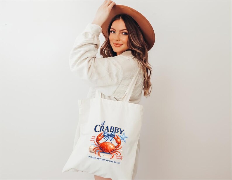 May include: A white tote bag with a crab illustration and the text "if Crabby, Please Return to the Beach." The crab is red and orange with blue accents. The bag has long handles.