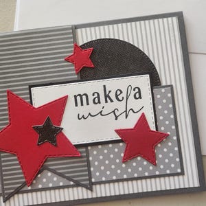 May include: A gray and white card with a red and black star design. The card has the text "make a wish" on it.