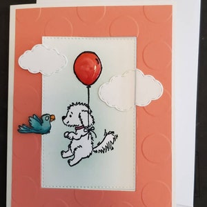 May include: A greeting card with a peach background featuring a white dog holding a red balloon. The dog is surrounded by white clouds and a blue bird. The card has a white border.