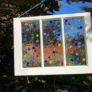 May include: A white painted window frame with three panes of glass. Each pane is decorated with colourful glass marbles.