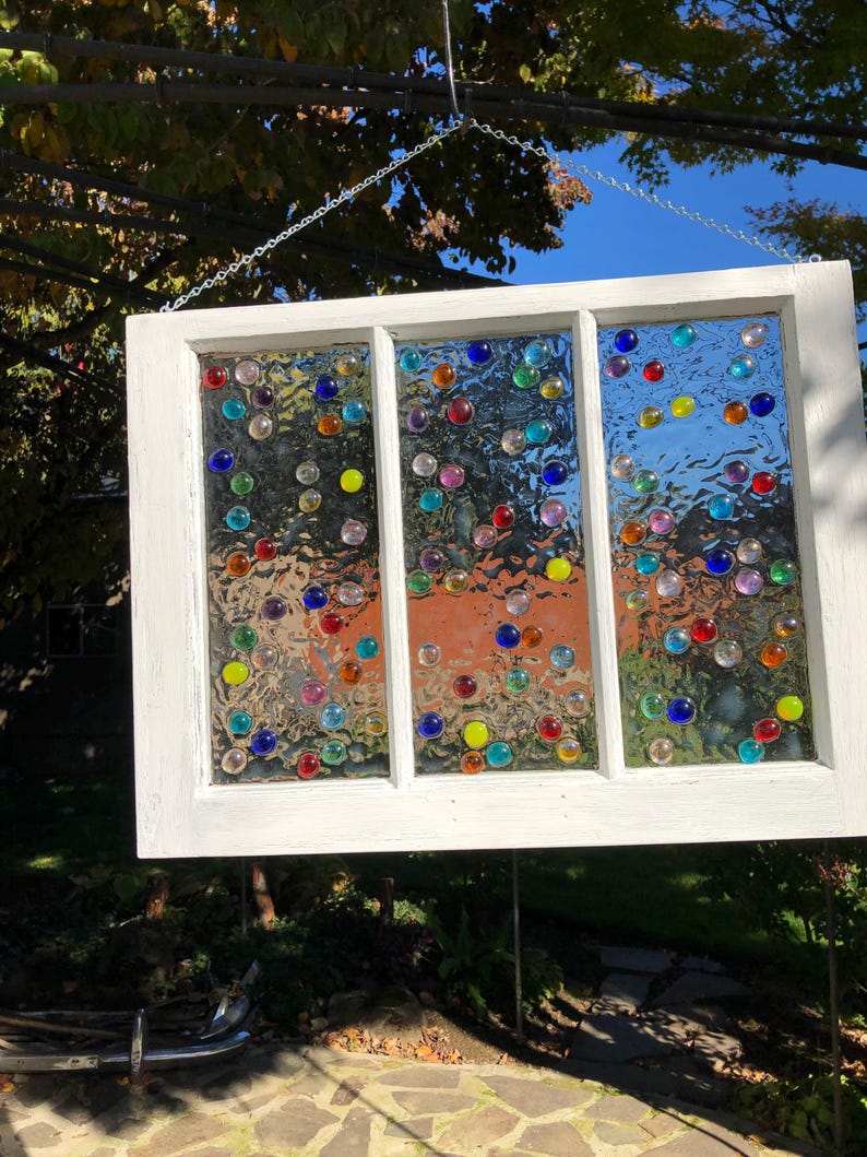 May include: A white painted window frame with three panes of glass. Each pane is decorated with colourful glass marbles.