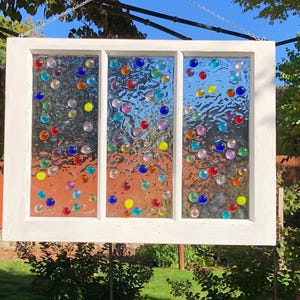 May include: A white window frame with three panes of glass, each filled with colorful glass beads. The beads are arranged in a random pattern and create a whimsical and colorful design.