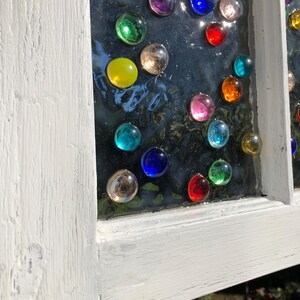 May include: A white painted window frame with a glass pane featuring a colourful mosaic of round glass gems. The gems are arranged in a circular pattern and include shades of red, blue, green, yellow, and purple.