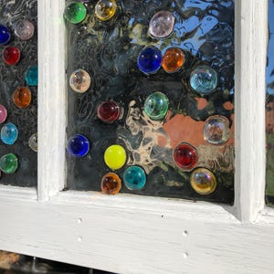May include: A white painted window frame with a glass pane decorated with colourful glass gems. The gems are arranged in a random pattern and are various shapes and sizes.