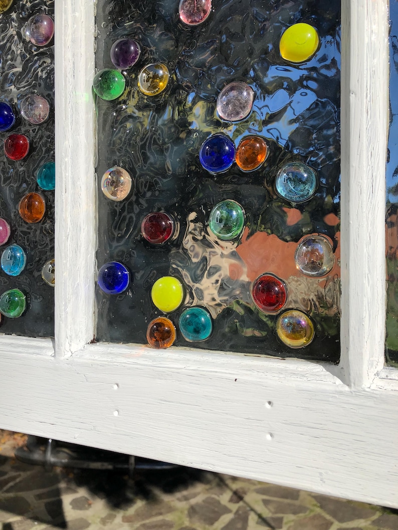 May include: A white painted window frame with a glass pane decorated with colourful glass gems. The gems are arranged in a random pattern and are various shapes and sizes.