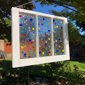 May include: A white painted window frame with three panes of glass. Each pane is decorated with colourful glass marbles.