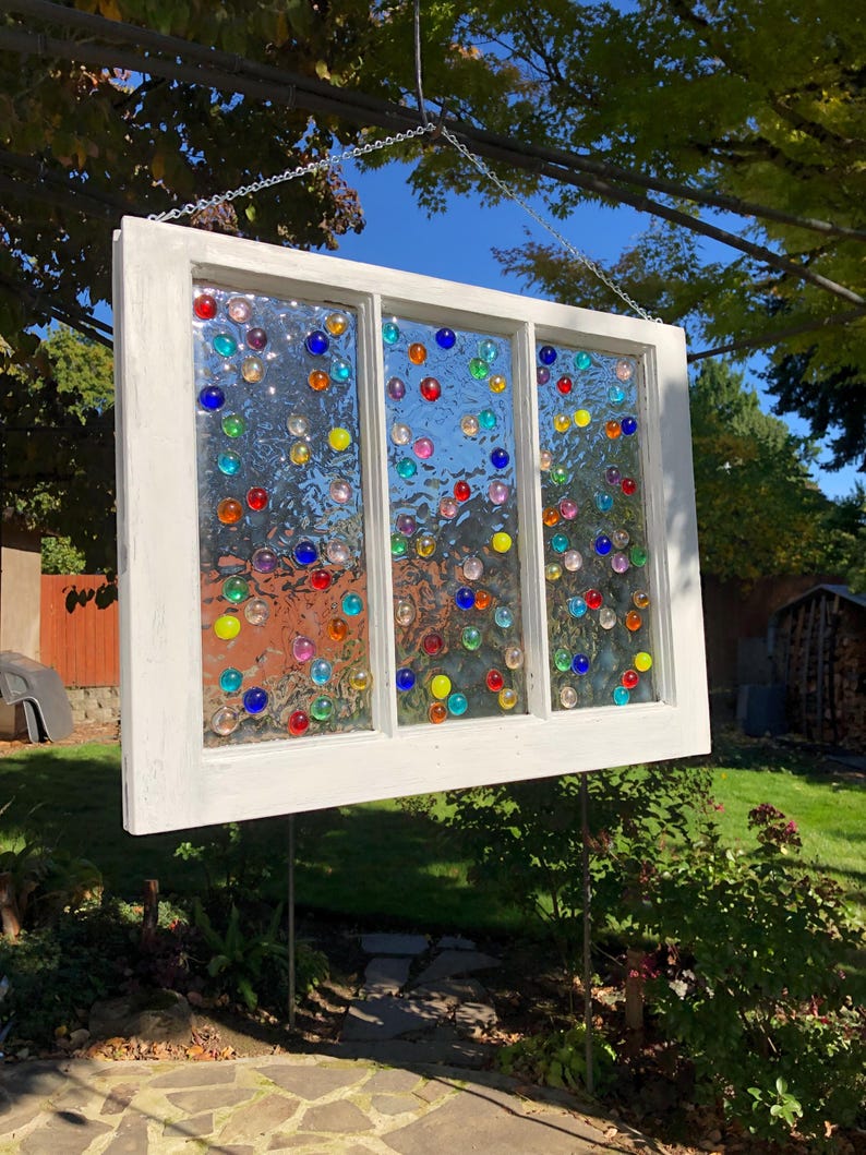 May include: A white painted window frame with three panes of glass. Each pane is decorated with colourful glass marbles.