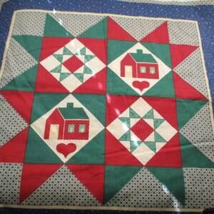 Könnte beinhalten: Eine rote, grüne und weiße Patchwork-Decke mit einem Sternmuster. Die Decke zeigt zwei rote Häuser mit weißen Fenstern und einem weißen Herzen.