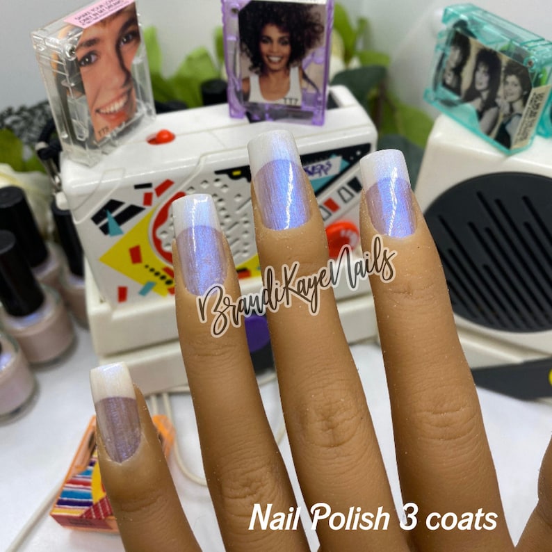 Peut inclure: Main montrant de longs ongles carr&eacute;s vernis d'un vernis nacr&eacute; et iris&eacute;. Les pointes sont blanches et la couleur de base oscille entre le bleu et le violet. Le texte "Nail Polish 3 coats" est en bas et la marque "BrandiKayeNails" est au centre.