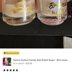 Peut inclure: Deux flacons de vernis &agrave; ongles iris&eacute;s. L'un porte l'inscription "77 Cotton Candy Sati" en lettres dor&eacute;es. L'autre porte l'inscription "Branda NAIL LAC 0,51 oz" en lettres dor&eacute;es.