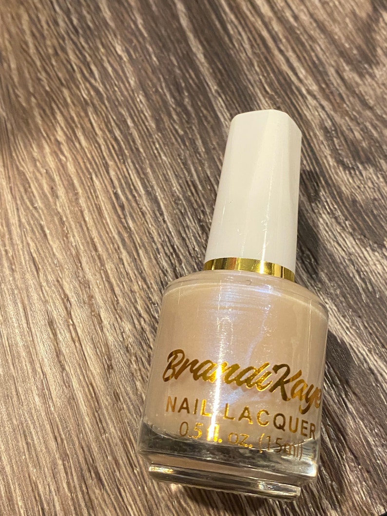 Peut inclure: Un flacon de vernis &agrave; ongles Brandi Raye. Le vernis est de couleur beige clair avec un &eacute;clat nacr&eacute;. Le flacon a un bouchon blanc et des accents dor&eacute;s. L'&eacute;tiquette indique "Brandi Raye NAIL LACQUER 0.5 fl. oz. (15ml)".