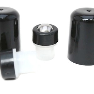 May include: A collection of black roller bottle caps and roller ball inserts. The caps are cylindrical and glossy. The roller ball inserts have a clear plastic base and a silver metal ball. The items are on a white background.